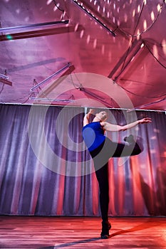 Flexible beautiful gymnast girl doing gymnastic exercises in the hall or on the stage. Young woman jumping in sport dress.