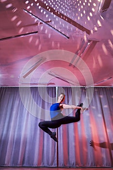 Flexible beautiful gymnast girl doing gymnastic exercises in the hall or on the stage. Young woman jumping in sport dress.