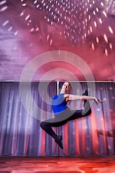 Flexible beautiful gymnast girl doing gymnastic exercises in the hall or on the stage. Young woman jumping in sport dress.