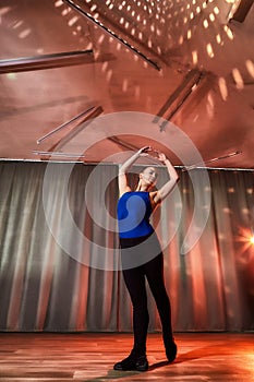 Flexible beautiful gymnast girl standing in the hall or on the stage with interesting light. Portrait of young woman in sport