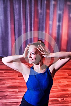 Flexible beautiful gymnast girl standing in the hall or on the stage with interesting light. Portrait of young woman in sport