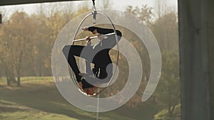 Flexible brunette with bare feet hanging in ring for aerial acrobatics in slo-mo