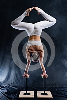 Flexible circus artist - female acrobat doing handstand on the back and smoker background. concept of willpower and