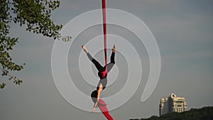 Flexible female acrobat doing crazy and dangerous trick on red aerial silk the sunset sky background is slow motion