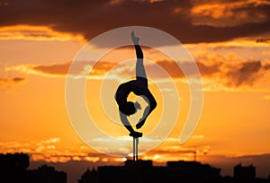 Flexible female circus Artist keep balance and doing contortion on the rooftop against dramatic sunset and cityscape