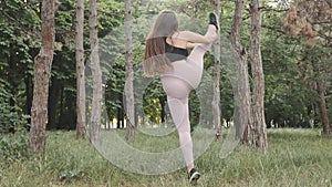 Flexible female gymnast doing acrobatic tricks in the park, slow motion