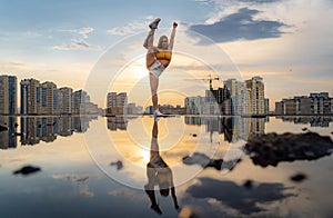 Flexible female gymnast making trick with reflection in the water during dramatic sunset