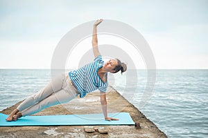 Flexible fitness woman yoga instructor practicing vasishthasana posture on beach dock seaside