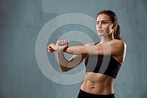 Flexible fitnesswoman stretching arm before training.