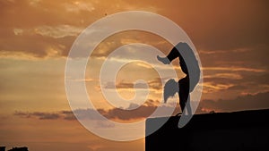 Flexible girl doing handstand on sky background during dramatic sunset in slow motion