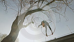 Flexible gymnastics woman performs acrobatics tricks on aerial hoop outdoors