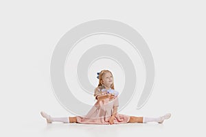 Flexible little cute girl, kid in retro fashion outfit sitting in twine isolated on white background. Concept of kids