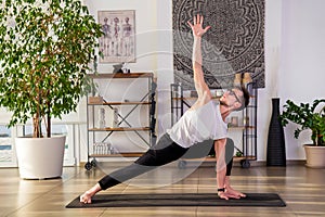 Flexible man performing revolved lunge yoga pose in studio