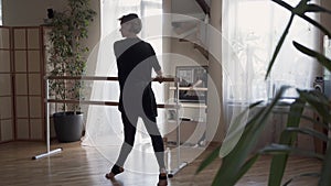 Flexible mature woman dancing at home in front of the mirror. Elegant slim woman in black clothes doing exercises