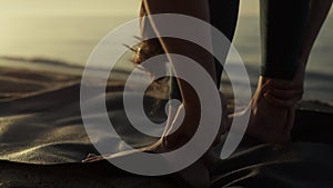 Flexible sportswoman bending body to feet on beach closeup. Yoga woman training
