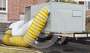 Flexible tubing attached to huge industrial vacuum running to brick building.