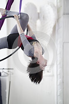 Flexible woman gymnast hangs upside down on the aerial hoop