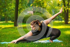 flexible woman plus size in the park on the lawn performs stretching