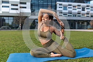 Flexible young black woman doing yoga pigeon pose during outdoor practice at city park, copy space