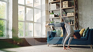Flexible young woman is exercising at home practising yoga asanas on floor of modern apartment stretching body, arms and