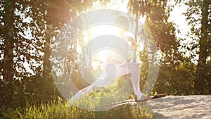 Flexible young woman exercising yoga pose of warrior background of beautiful bright sunray and trees