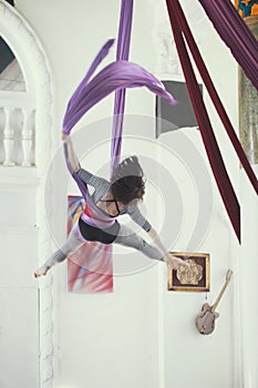 Flexible young woman flying on the aerial silk is a bright studio