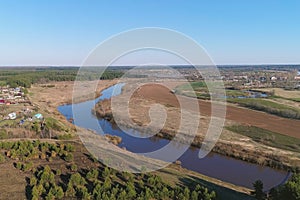 Flight above green fields, forest, river and village early spring, aerial panoramic view photo.