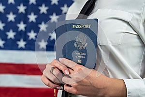 flight attendant holding fan of dollars and passport and standing against an flag background.