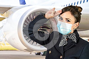 A flight attendant poses in her uniform and surgical mask in front of an airplane turbine. Subject on a blurred background