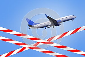 Flight ban. Crossed barrier tapes with red and white stripes against the background of a flying plane