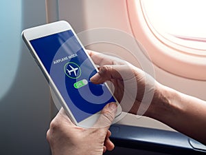 Flight mode concept. Hand holding white smartphone and turned on airplane mode on screen near the window on the airplane