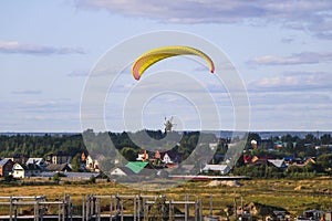 Flight of motor paraplan. a man flies on a bright colorful motoparaplane above the village, field and construction site.