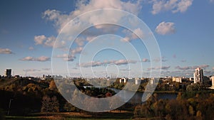 Flight over the autumn park. Park on the shore of a large lake. On the horizon there is a blue sky and city houses. Trees with yel