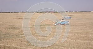 Flight over a field with a combine harvester that collects wheat, view from a drone