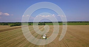 Flight over a field with a combine harvester that collects wheat, view from a drone