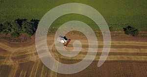 Flight over a field with a combine harvester that collects wheat, view from a drone