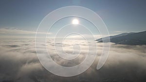 Flight over the fog between the mountains. Clouds during beautiful morning sunrise with flare light over the Carpathian