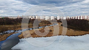 Flight over the river in the spring park. Remnants of ice are visible. In the distance, people are walking along the alleys