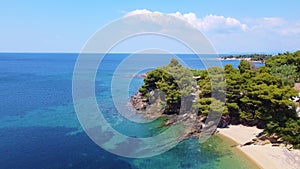 Flight over the rocky coast with green trees and blue transparent sea. Aerial view