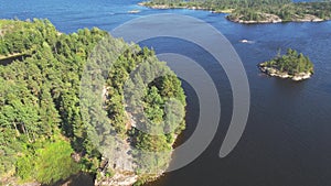 Flight over a rocky islands covered with a green coniferous forest. Coastal zone of Lake Ladoga