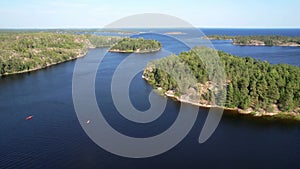 Flight over a rocky islands covered with a green coniferous forest. Two small orange kayaks on the water