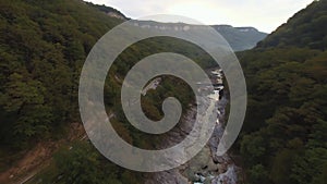 Flight over a rural landscape road following a car driving on it with lush green foliage, farming land. Aerial shot of a