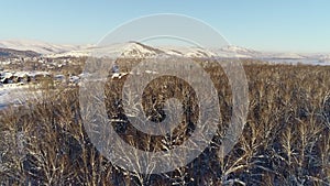 Flight over the winter forest to the mountains on a sunny morning. A village on the banks of a winter river. Winter