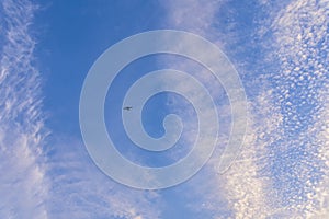 Flight of a twin-engine plane high in the sky against a blue sky and clouds
