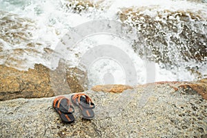 Flip flop on stone with splash wave white water at coast of sea ocean.