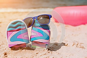 Flip-flops in sand on beach. Sunglasses on it. Summer vacation concept. Sea shore. Paradise. Pink swimming ring lying
