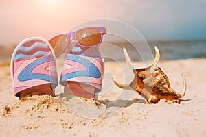 Flip-flops in sand on beach. Sunglasses on it. Summer vacation concept. Sea shore. Paradise. Sea shell lying on sand.