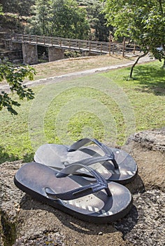 Flip-flops sandal over rocks beside grass recreation area of Acebo natural swimming pool photo