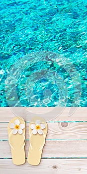 Flip flops with tiare flowers on the wooden planks decking above turquoise sea blurred background