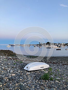 Flipped boat on the rocky shore against the background of the coast with vessels. Rye Harbor Beach.